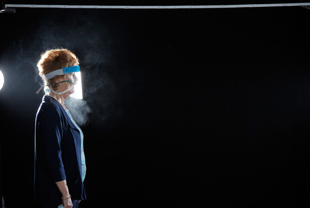 Mischa Nawrata, Fotograf, Aerosolausstoßtest, Chorverband Österreich, Aerosolausstoßtestung, Prof. Dr. Fritz Sterz, Ao.Univ.-Prof. Dr.med.univ. Fritz Sterz, fritz.sterz@meduniwien.ac.at , MedUni Wien, Universitätskliniken der MedUni Wien / AKH Wien, ao.Univ.Prof. Dr. Harald Herkner, MSc, Dr. Heinz Bixa, DDr. Karl-Gerhard Straßl MAS, Präsident, Chorverband Österreich, Mit 4-8 Liter Sauerstoff pro Minute wurde mit einer Düse in einem kleinen Behältnis mit 0,9% Kochsalz Nebel (= Aerosol) erzeugt. Mit kleinen Sonden in den Nasenöffnungen wurde den Sängern dieser Nebel kontinuierlich zusätzlich zum Atmen verabreicht. Die Verstreuung des Aerosols in den oberen Atemwegen war damit gewährleistet. In einem schwarz ausgekleideten Raum befanden sich hinter dem jeweiligen Musiker links und rechts besonders starke Scheinwerfer, um das Ausströmen der Aerosole sichtbar zu machen. Dadurch war es möglich, die Verteilung der Ausatmungsluft im Gegenlicht zu visualisieren und fotographisch zu dokumentieren, ChVOe=Chorverband Österreich, Alt, Tenor, Bass, oM=ohne Maske, mM=mit Maske, mG=mit Gesichtsschutz, mMprivat=private Schutzmaske aus Stoff genäht, FFP2 Schutzmaske, es wurden Vokale und Konsonanten gesungen,