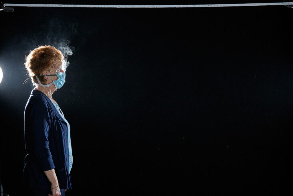 Mischa Nawrata, Fotograf, Aerosolausstoßtest, Chorverband Österreich, Aerosolausstoßtestung, Prof. Dr. Fritz Sterz, Ao.Univ.-Prof. Dr.med.univ. Fritz Sterz, fritz.sterz@meduniwien.ac.at , MedUni Wien, Universitätskliniken der MedUni Wien / AKH Wien, ao.Univ.Prof. Dr. Harald Herkner, MSc, Dr. Heinz Bixa, DDr. Karl-Gerhard Straßl MAS, Präsident, Chorverband Österreich, Mit 4-8 Liter Sauerstoff pro Minute wurde mit einer Düse in einem kleinen Behältnis mit 0,9% Kochsalz Nebel (= Aerosol) erzeugt. Mit kleinen Sonden in den Nasenöffnungen wurde den Sängern dieser Nebel kontinuierlich zusätzlich zum Atmen verabreicht. Die Verstreuung des Aerosols in den oberen Atemwegen war damit gewährleistet. In einem schwarz ausgekleideten Raum befanden sich hinter dem jeweiligen Musiker links und rechts besonders starke Scheinwerfer, um das Ausströmen der Aerosole sichtbar zu machen. Dadurch war es möglich, die Verteilung der Ausatmungsluft im Gegenlicht zu visualisieren und fotographisch zu dokumentieren, ChVOe=Chorverband Österreich, Alt, Tenor, Bass, oM=ohne Maske, mM=mit Maske, mG=mit Gesichtsschutz, mMprivat=private Schutzmaske aus Stoff genäht, FFP2 Schutzmaske, es wurden Vokale und Konsonanten gesungen,