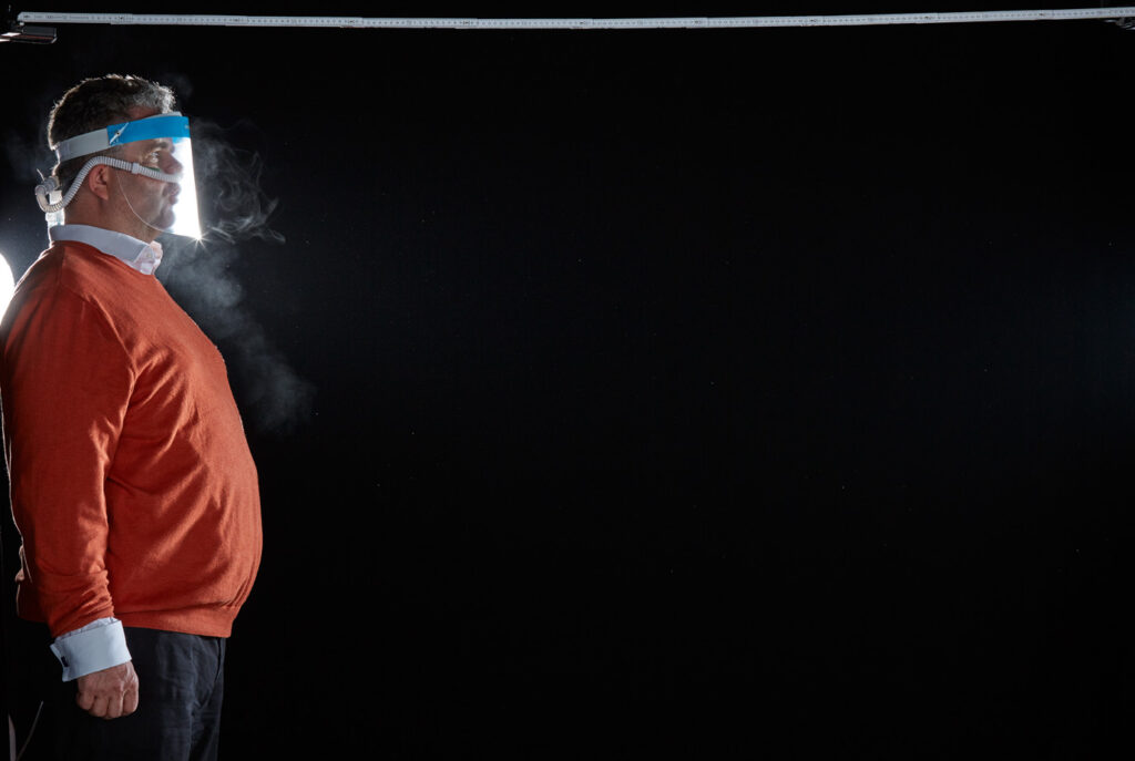 Mischa Nawrata, Fotograf, Aerosolausstoßtest, Chorverband Österreich, Aerosolausstoßtestung, Prof. Dr. Fritz Sterz, Ao.Univ.-Prof. Dr.med.univ. Fritz Sterz, fritz.sterz@meduniwien.ac.at , MedUni Wien, Universitätskliniken der MedUni Wien / AKH Wien, ao.Univ.Prof. Dr. Harald Herkner, MSc, Dr. Heinz Bixa, DDr. Karl-Gerhard Straßl MAS, Präsident, Chorverband Österreich, Mit 4-8 Liter Sauerstoff pro Minute wurde mit einer Düse in einem kleinen Behältnis mit 0,9% Kochsalz Nebel (= Aerosol) erzeugt. Mit kleinen Sonden in den Nasenöffnungen wurde den Sängern dieser Nebel kontinuierlich zusätzlich zum Atmen verabreicht. Die Verstreuung des Aerosols in den oberen Atemwegen war damit gewährleistet. In einem schwarz ausgekleideten Raum befanden sich hinter dem jeweiligen Musiker links und rechts besonders starke Scheinwerfer, um das Ausströmen der Aerosole sichtbar zu machen. Dadurch war es möglich, die Verteilung der Ausatmungsluft im Gegenlicht zu visualisieren und fotographisch zu dokumentieren, ChVOe=Chorverband Österreich, Alt, Tenor, Bass, oM=ohne Maske, mM=mit Maske, mG=mit Gesichtsschutz, mMprivat=private Schutzmaske aus Stoff genäht, FFP2 Schutzmaske, es wurden Vokale und Konsonanten gesungen,