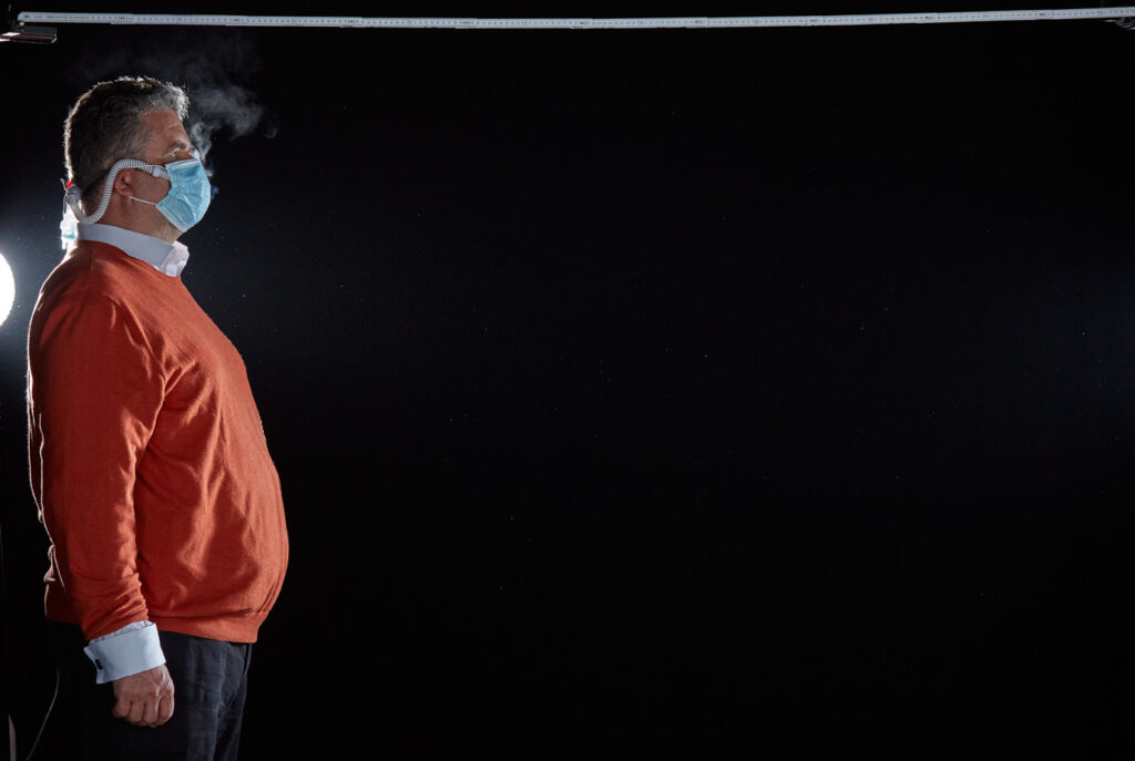 Mischa Nawrata, Fotograf, Aerosolausstoßtest, Chorverband Österreich, Aerosolausstoßtestung, Prof. Dr. Fritz Sterz, Ao.Univ.-Prof. Dr.med.univ. Fritz Sterz, fritz.sterz@meduniwien.ac.at , MedUni Wien, Universitätskliniken der MedUni Wien / AKH Wien, ao.Univ.Prof. Dr. Harald Herkner, MSc, Dr. Heinz Bixa, DDr. Karl-Gerhard Straßl MAS, Präsident, Chorverband Österreich, Mit 4-8 Liter Sauerstoff pro Minute wurde mit einer Düse in einem kleinen Behältnis mit 0,9% Kochsalz Nebel (= Aerosol) erzeugt. Mit kleinen Sonden in den Nasenöffnungen wurde den Sängern dieser Nebel kontinuierlich zusätzlich zum Atmen verabreicht. Die Verstreuung des Aerosols in den oberen Atemwegen war damit gewährleistet. In einem schwarz ausgekleideten Raum befanden sich hinter dem jeweiligen Musiker links und rechts besonders starke Scheinwerfer, um das Ausströmen der Aerosole sichtbar zu machen. Dadurch war es möglich, die Verteilung der Ausatmungsluft im Gegenlicht zu visualisieren und fotographisch zu dokumentieren, ChVOe=Chorverband Österreich, Alt, Tenor, Bass, oM=ohne Maske, mM=mit Maske, mG=mit Gesichtsschutz, mMprivat=private Schutzmaske aus Stoff genäht, FFP2 Schutzmaske, es wurden Vokale und Konsonanten gesungen,