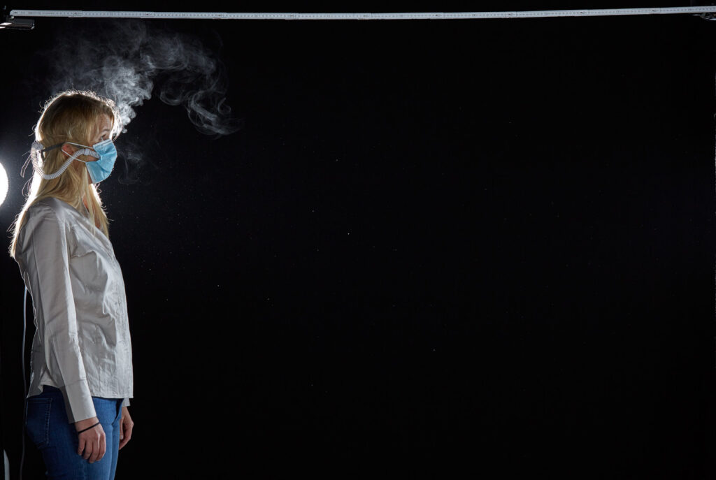 Mischa Nawrata, Fotograf, Aerosolausstoßtest, Chorverband Österreich, Aerosolausstoßtestung, Prof. Dr. Fritz Sterz, Ao.Univ.-Prof. Dr.med.univ. Fritz Sterz, fritz.sterz@meduniwien.ac.at , MedUni Wien, Universitätskliniken der MedUni Wien / AKH Wien, ao.Univ.Prof. Dr. Harald Herkner, MSc, Dr. Heinz Bixa, DDr. Karl-Gerhard Straßl MAS, Präsident, Chorverband Österreich, Mit 4-8 Liter Sauerstoff pro Minute wurde mit einer Düse in einem kleinen Behältnis mit 0,9% Kochsalz Nebel (= Aerosol) erzeugt. Mit kleinen Sonden in den Nasenöffnungen wurde den Sängern dieser Nebel kontinuierlich zusätzlich zum Atmen verabreicht. Die Verstreuung des Aerosols in den oberen Atemwegen war damit gewährleistet. In einem schwarz ausgekleideten Raum befanden sich hinter dem jeweiligen Musiker links und rechts besonders starke Scheinwerfer, um das Ausströmen der Aerosole sichtbar zu machen. Dadurch war es möglich, die Verteilung der Ausatmungsluft im Gegenlicht zu visualisieren und fotographisch zu dokumentieren, ChVOe=Chorverband Österreich, Alt, Tenor, Bass, oM=ohne Maske, mM=mit Maske, mG=mit Gesichtsschutz, mMprivat=private Schutzmaske aus Stoff genäht, FFP2 Schutzmaske, es wurden Vokale und Konsonanten gesungen,