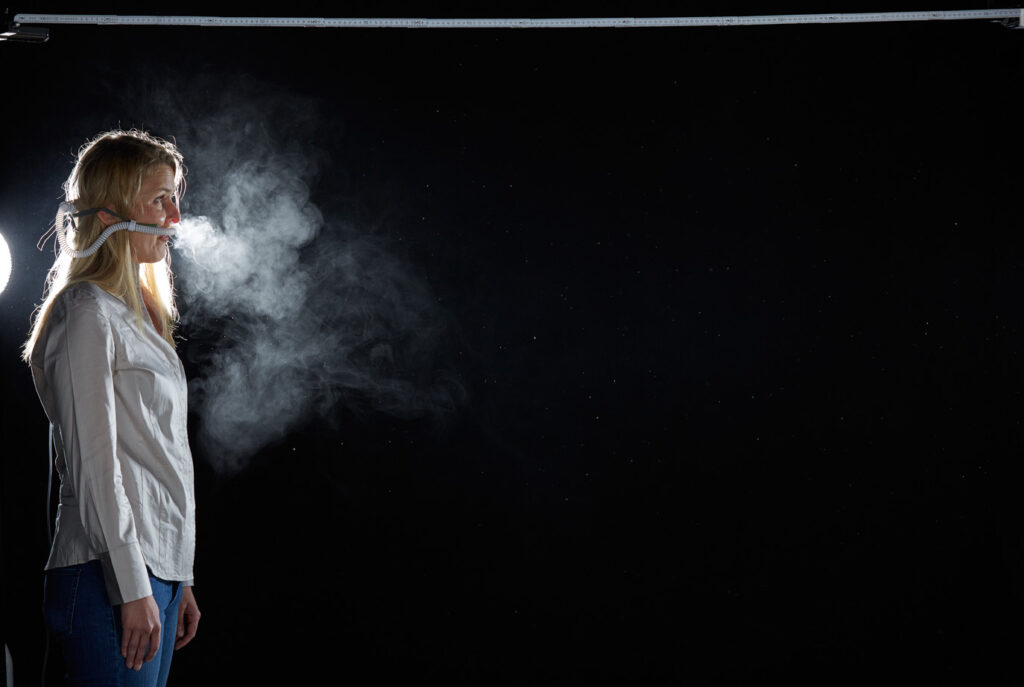 Mischa Nawrata, Fotograf, Aerosolausstoßtest, Chorverband Österreich, Aerosolausstoßtestung, Prof. Dr. Fritz Sterz, Ao.Univ.-Prof. Dr.med.univ. Fritz Sterz, fritz.sterz@meduniwien.ac.at , MedUni Wien, Universitätskliniken der MedUni Wien / AKH Wien, ao.Univ.Prof. Dr. Harald Herkner, MSc, Dr. Heinz Bixa, DDr. Karl-Gerhard Straßl MAS, Präsident, Chorverband Österreich, Mit 4-8 Liter Sauerstoff pro Minute wurde mit einer Düse in einem kleinen Behältnis mit 0,9% Kochsalz Nebel (= Aerosol) erzeugt. Mit kleinen Sonden in den Nasenöffnungen wurde den Sängern dieser Nebel kontinuierlich zusätzlich zum Atmen verabreicht. Die Verstreuung des Aerosols in den oberen Atemwegen war damit gewährleistet. In einem schwarz ausgekleideten Raum befanden sich hinter dem jeweiligen Musiker links und rechts besonders starke Scheinwerfer, um das Ausströmen der Aerosole sichtbar zu machen. Dadurch war es möglich, die Verteilung der Ausatmungsluft im Gegenlicht zu visualisieren und fotographisch zu dokumentieren, ChVOe=Chorverband Österreich, Alt, Tenor, Bass, oM=ohne Maske, mM=mit Maske, mG=mit Gesichtsschutz, mMprivat=private Schutzmaske aus Stoff genäht, FFP2 Schutzmaske, es wurden Vokale und Konsonanten gesungen,