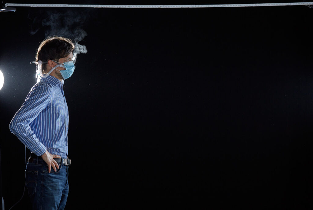 Mischa Nawrata, Fotograf, Aerosolausstoßtest, Chorverband Österreich, Aerosolausstoßtestung, Prof. Dr. Fritz Sterz, Ao.Univ.-Prof. Dr.med.univ. Fritz Sterz, fritz.sterz@meduniwien.ac.at , MedUni Wien, Universitätskliniken der MedUni Wien / AKH Wien, ao.Univ.Prof. Dr. Harald Herkner, MSc, Dr. Heinz Bixa, DDr. Karl-Gerhard Straßl MAS, Präsident, Chorverband Österreich, Mit 4-8 Liter Sauerstoff pro Minute wurde mit einer Düse in einem kleinen Behältnis mit 0,9% Kochsalz Nebel (= Aerosol) erzeugt. Mit kleinen Sonden in den Nasenöffnungen wurde den Sängern dieser Nebel kontinuierlich zusätzlich zum Atmen verabreicht. Die Verstreuung des Aerosols in den oberen Atemwegen war damit gewährleistet. In einem schwarz ausgekleideten Raum befanden sich hinter dem jeweiligen Musiker links und rechts besonders starke Scheinwerfer, um das Ausströmen der Aerosole sichtbar zu machen. Dadurch war es möglich, die Verteilung der Ausatmungsluft im Gegenlicht zu visualisieren und fotographisch zu dokumentieren, ChVOe=Chorverband Österreich, Alt, Tenor, Bass, oM=ohne Maske, mM=mit Maske, mG=mit Gesichtsschutz, mMprivat=private Schutzmaske aus Stoff genäht, FFP2 Schutzmaske, es wurden Vokale und Konsonanten gesungen,